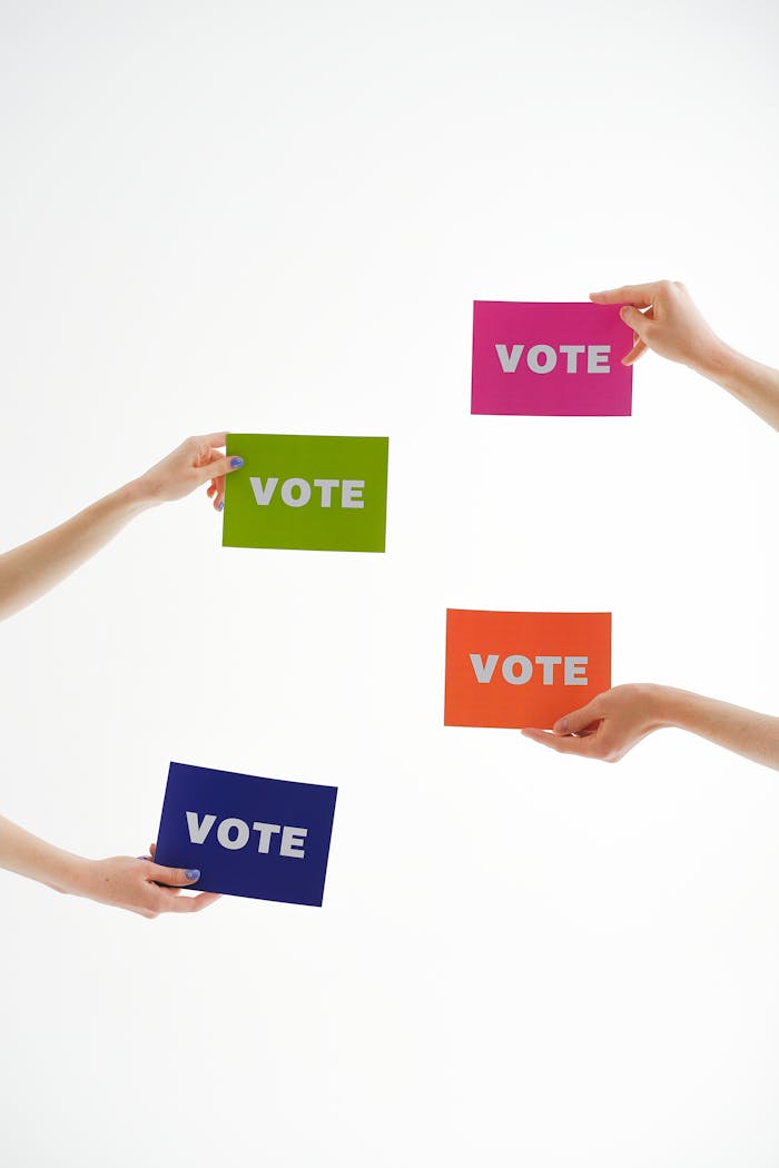Four hands holding colorful 'vote' cards, emphasizing democracy and participation.