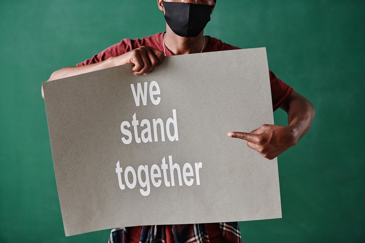 Person with face mask holding 'We stand together' sign against green background.