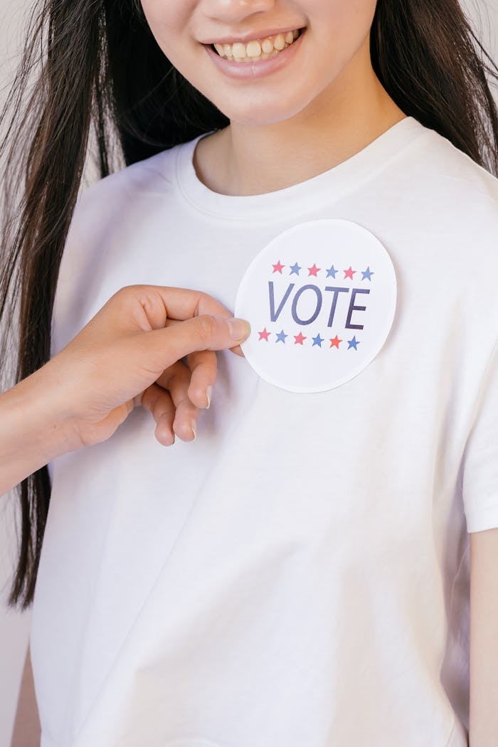 A person placing a round vote sticker on a white shirt, promoting political participation.